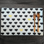 A set of four placemats with a black and yellow heart pattern on a white background, featuring a wooden fork and knife on top of the fabric.