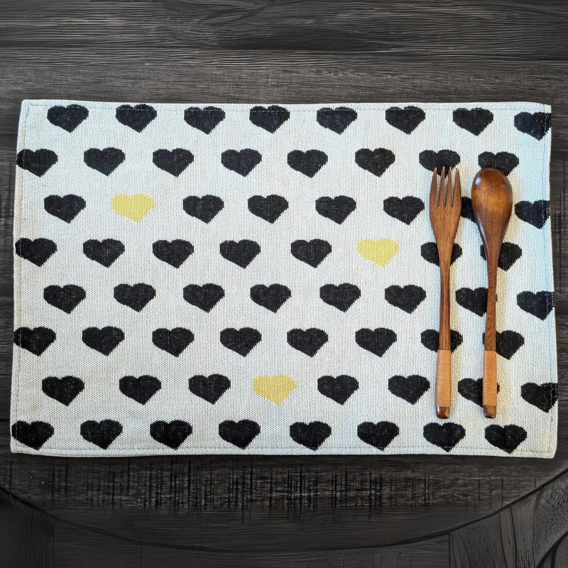A set of four placemats with a black and yellow heart pattern on a white background, featuring a wooden fork and knife on top of the fabric.