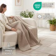 Woman sitting on a couch with a beige blanket, surrounded by plants and a 'OEKO-TEX' certified label.