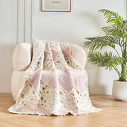 DaDalogy Floral Cottage Quilted Reversible Throw Blanket in blush pink and cream on a cozy chair with plants.