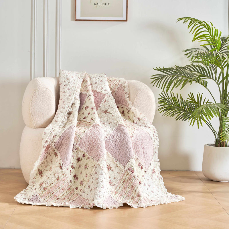 DaDalogy Floral Cottage Quilted Reversible Throw Blanket in blush pink and cream on a cozy chair with plants.