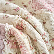 Close-up of DaDalogy Floral Cottage Patchwork Throw Blanket with pink and cream ruffles and botanical floral designs.