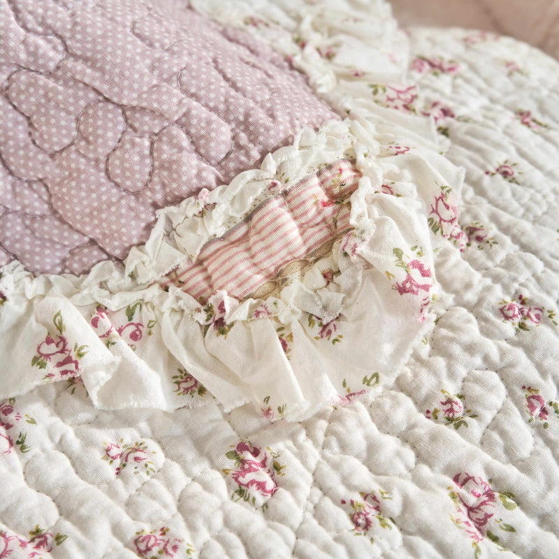 Close-up of DaDalogy Cotton Patchwork Throw Blanket featuring floral designs and ruffle details in blush pink and cream.