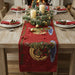 Dining table set for Christmas with a red table runner, candles, and decorative items.