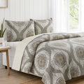 Bed with patterned bedding and pillows in a bright room with a window.