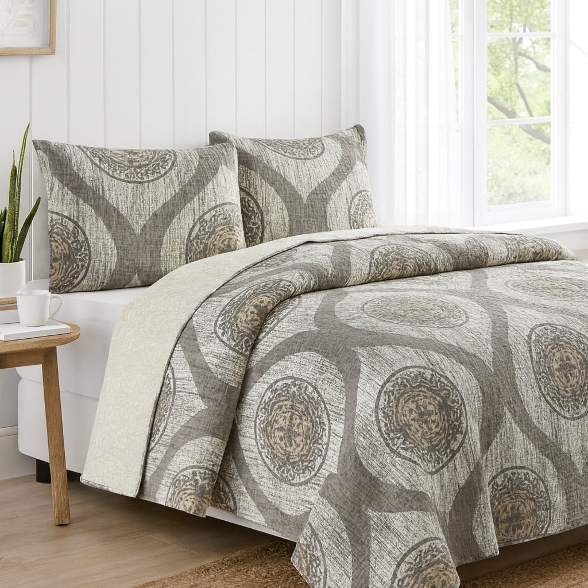 Bed with patterned bedding and pillows in a bright room with a window.