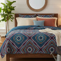 Bedroom with a bed featuring a patterned comforter and pillows, a plant, and a mirror on the wall.