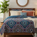 Bedroom with a bed featuring a patterned comforter and pillows, a plant, and a mirror on the wall.