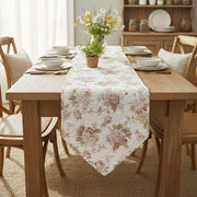 Dining table set with floral table runner, chairs, and a vase of flowers.
