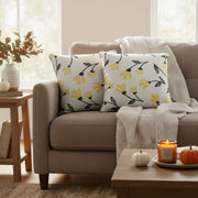 Beige sofa with floral-patterned pillows, a candle, and pumpkins in a cozy living room.