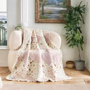 DaDalogy Cotton Patchwork Throw Blanket in blush pink and cream laid over a cozy chair, showcasing floral and ruffle design.